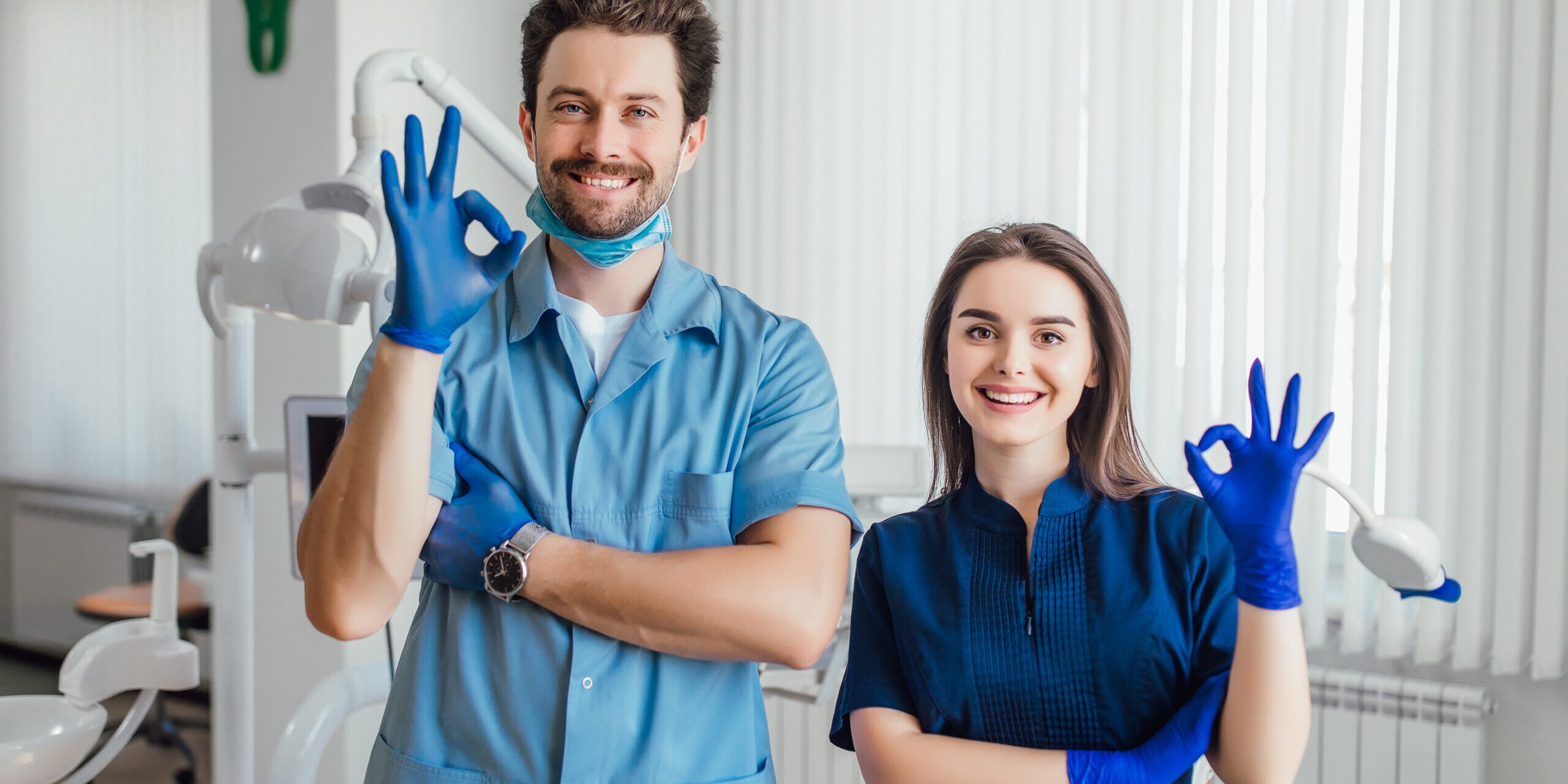 photo-smiling-dentist-standing-with-arms-crossed-with-her-colleague-showing-okay-sign